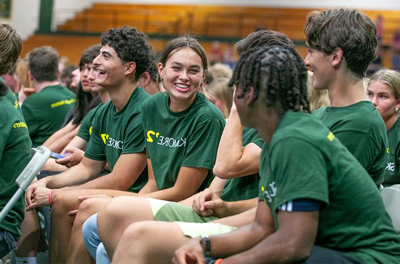 学生们穿着印有“火博体育”字样的绿色衬衫，坐在体育馆里互相问候
